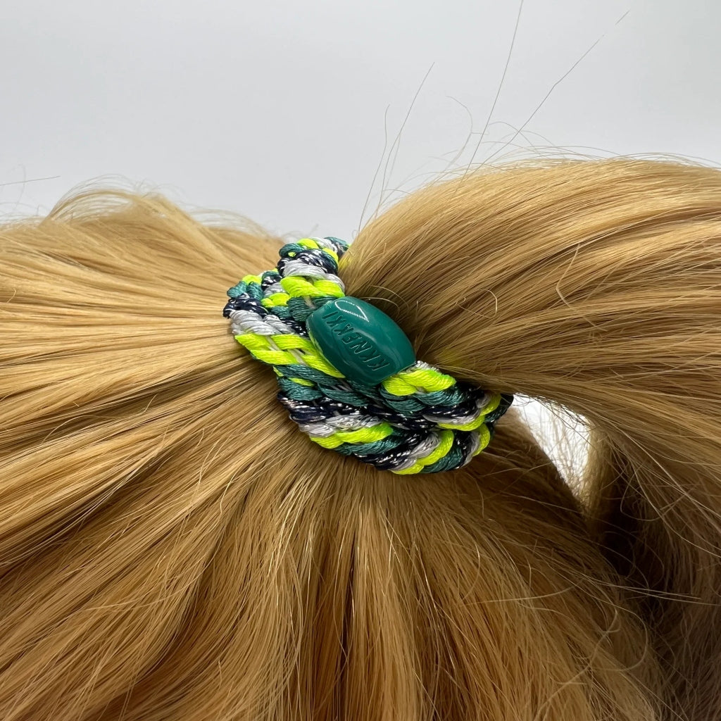 Hair tie with green and yellow pattern on a blonde ponytail against a white background